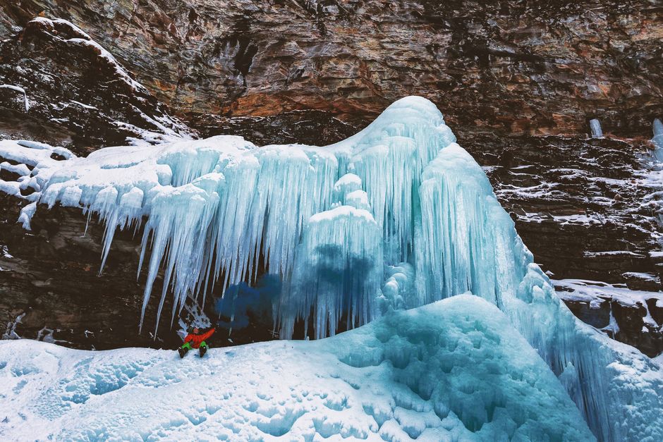 Daring ice climber tackles towering frozen waterfall in winter's icy embrace.