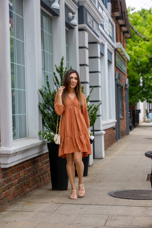Woman in Orange Dress Standing on Sidewalk