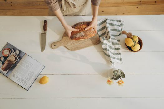 Hands preparing bread on a wooden board with fresh ingredients and a cookbook.