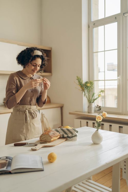Free Woman savoring freshly baked bread in a cozy kitchen setting with natural sunlight. Stock Photo