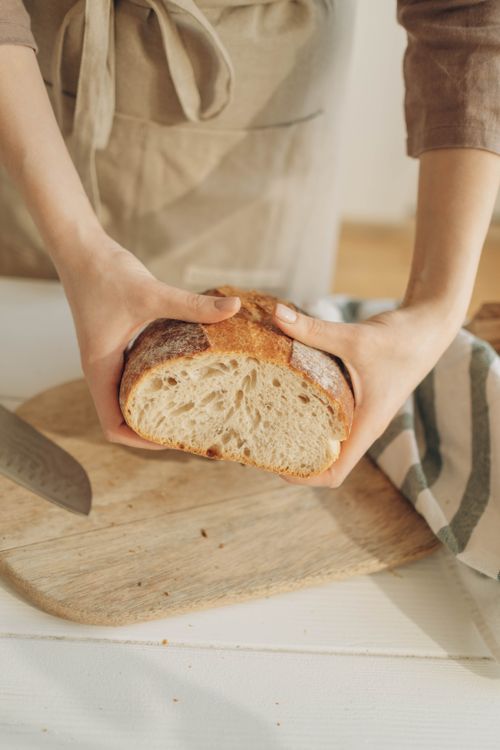 Free A close-up of hands holding a sliced artisan bread loaf on a wooden cutting board. Stock Photo