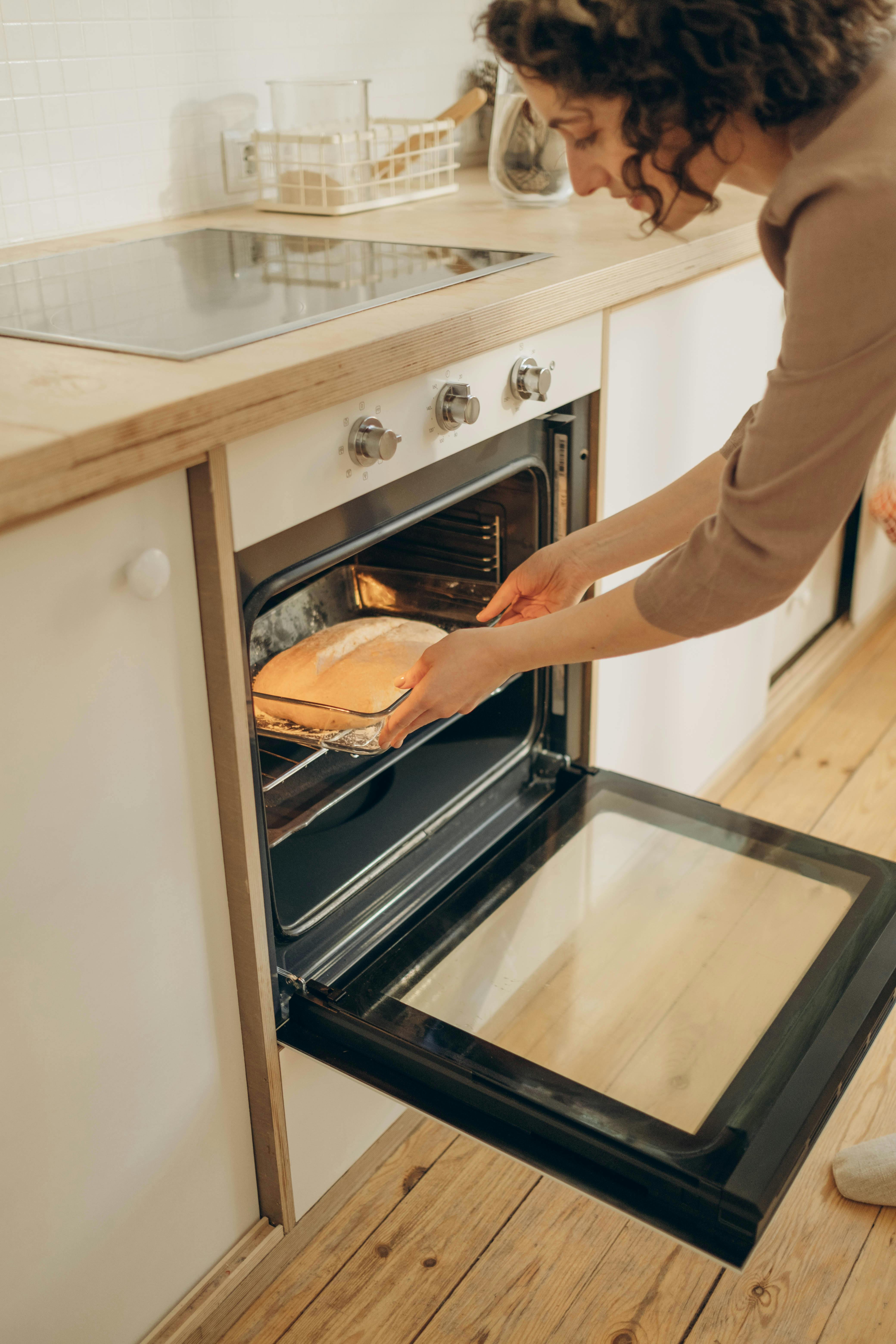 Adult woman placing bread in oven, showcasing home baking in a modern kitchen.