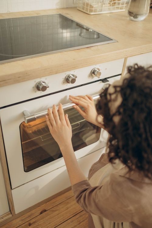 Free An adult woman with curly hair using a modern gas oven at home for baking. Stock Photo