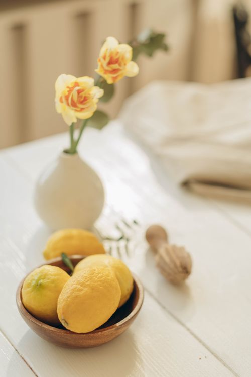 Free Artistic still life of lemons in a wooden bowl with flowers in a vase. Stock Photo