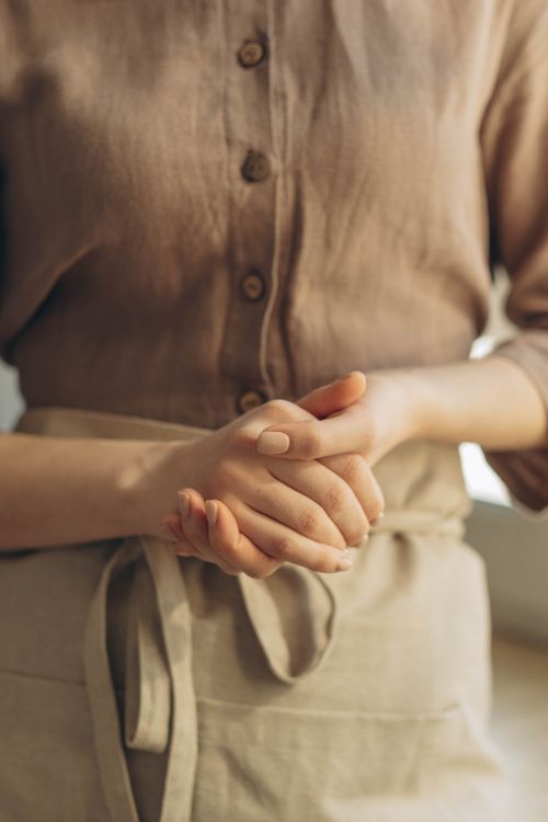 Hands folded over a washed linen apron in the workroom — photo by Ron Lach on Pexels