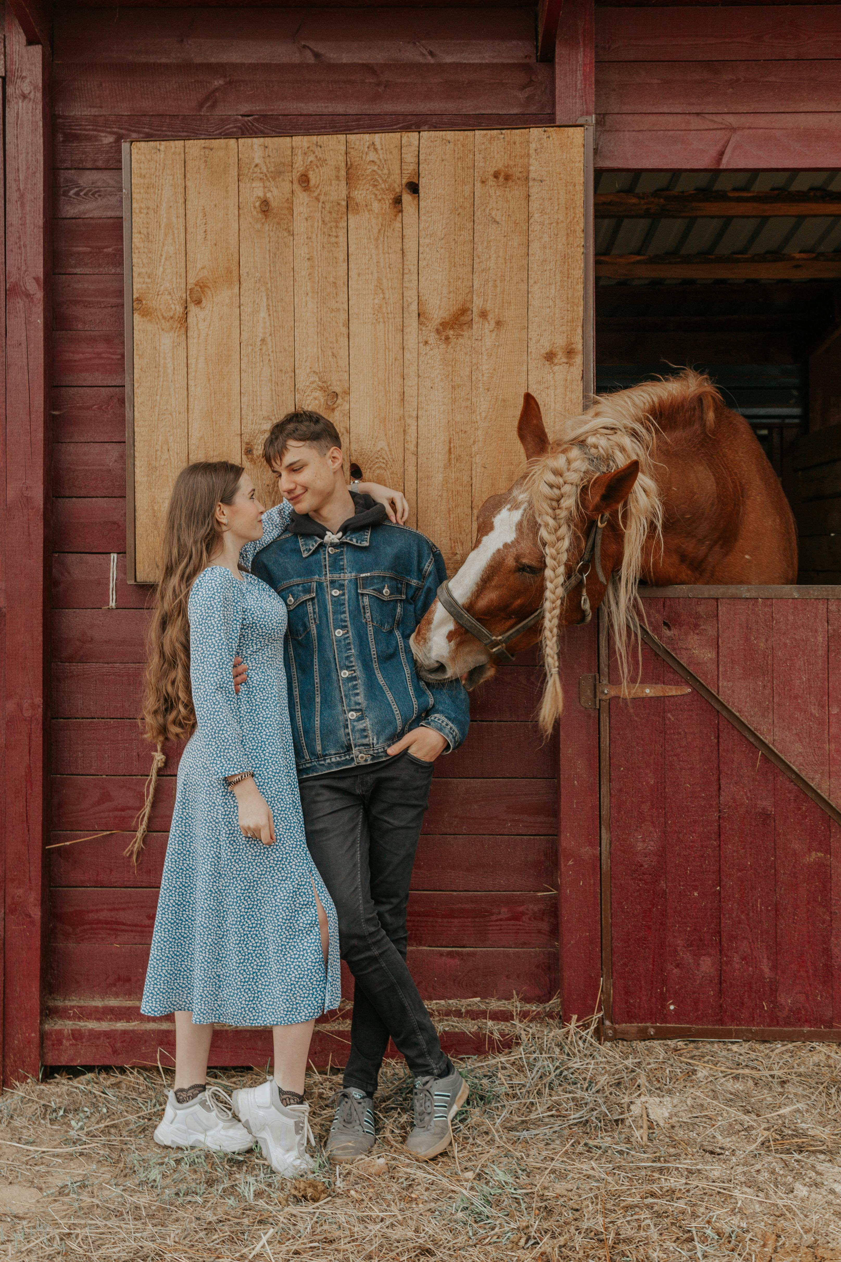 smiling couple embracing against horse peeping out of stable