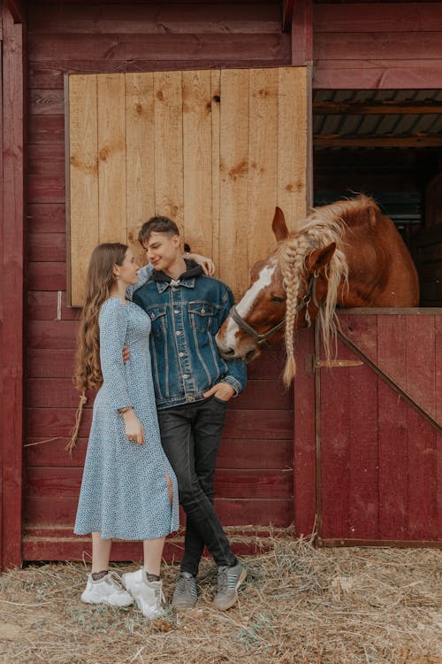 Smiling couple embracing against horse peeping out of stable
