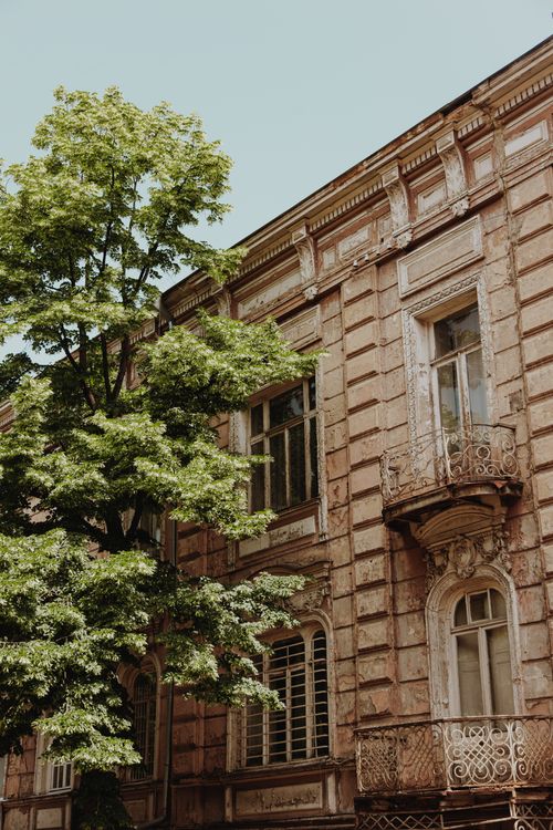 Free Elegant classic building facade with balconies and windows next to a lush green tree. Stock Photo