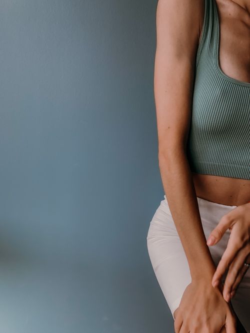 Free A cropped image of a person wearing a green tank top and beige pants against a teal wall. Stock Photo