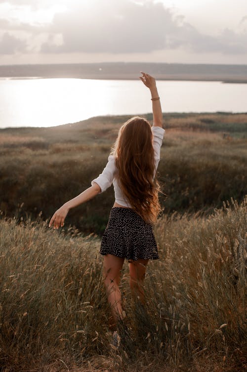 Woman in White Long Sleeve Shirt and Black and White Polka Dot Skirt Standing in Field