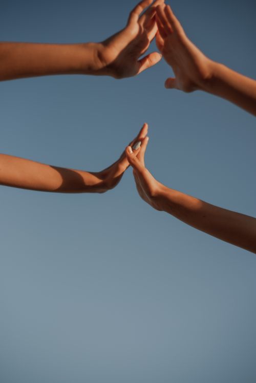 Free Multiple hands reaching together against a clear blue sky, symbolizing unity and teamwork. Stock Photo