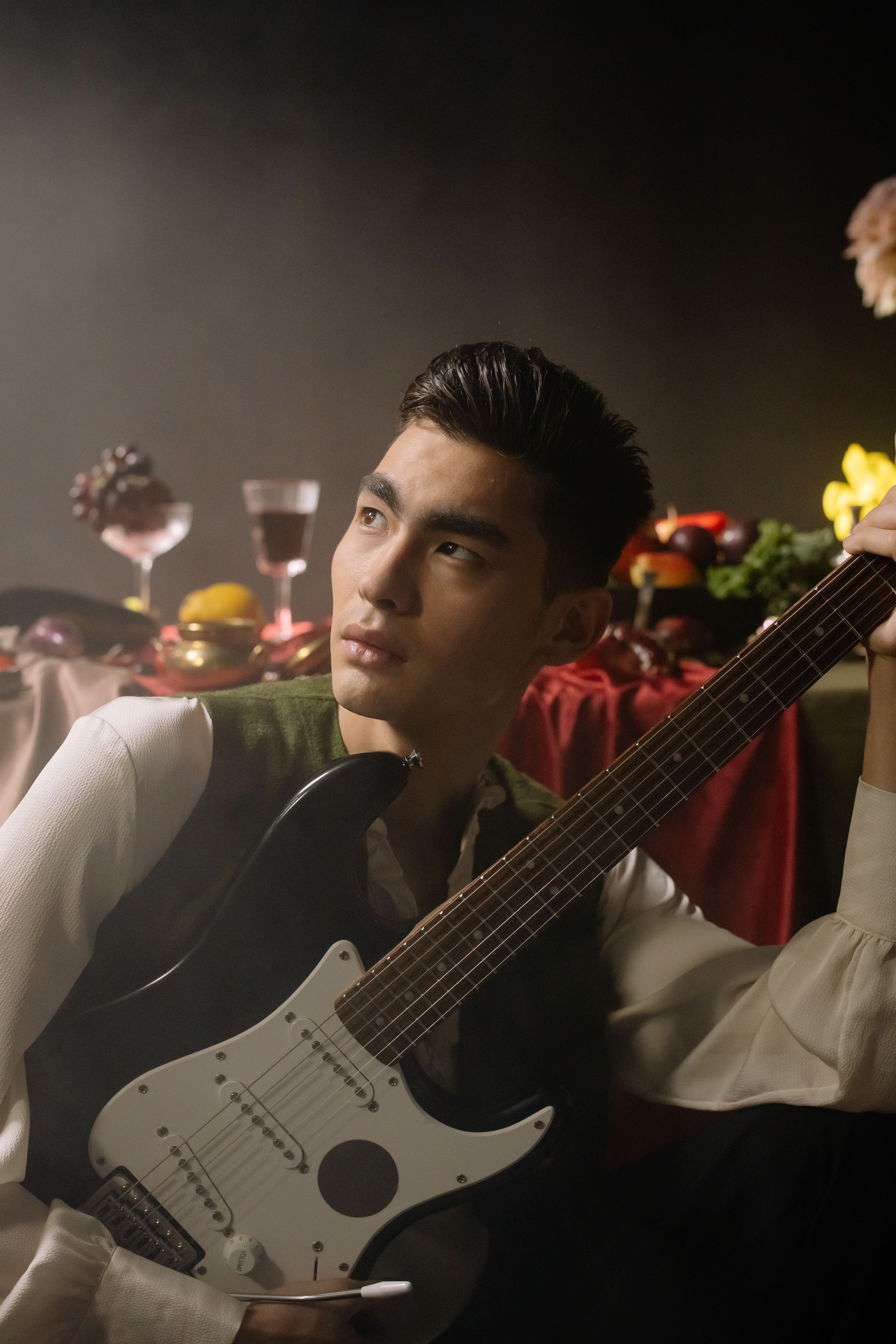 A young musician poses with an electric guitar in an artistic indoor setting.