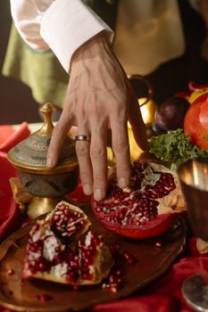 Close-up of a person's hand reaching for a ripe, juicy pomegranate on a decorative tray.