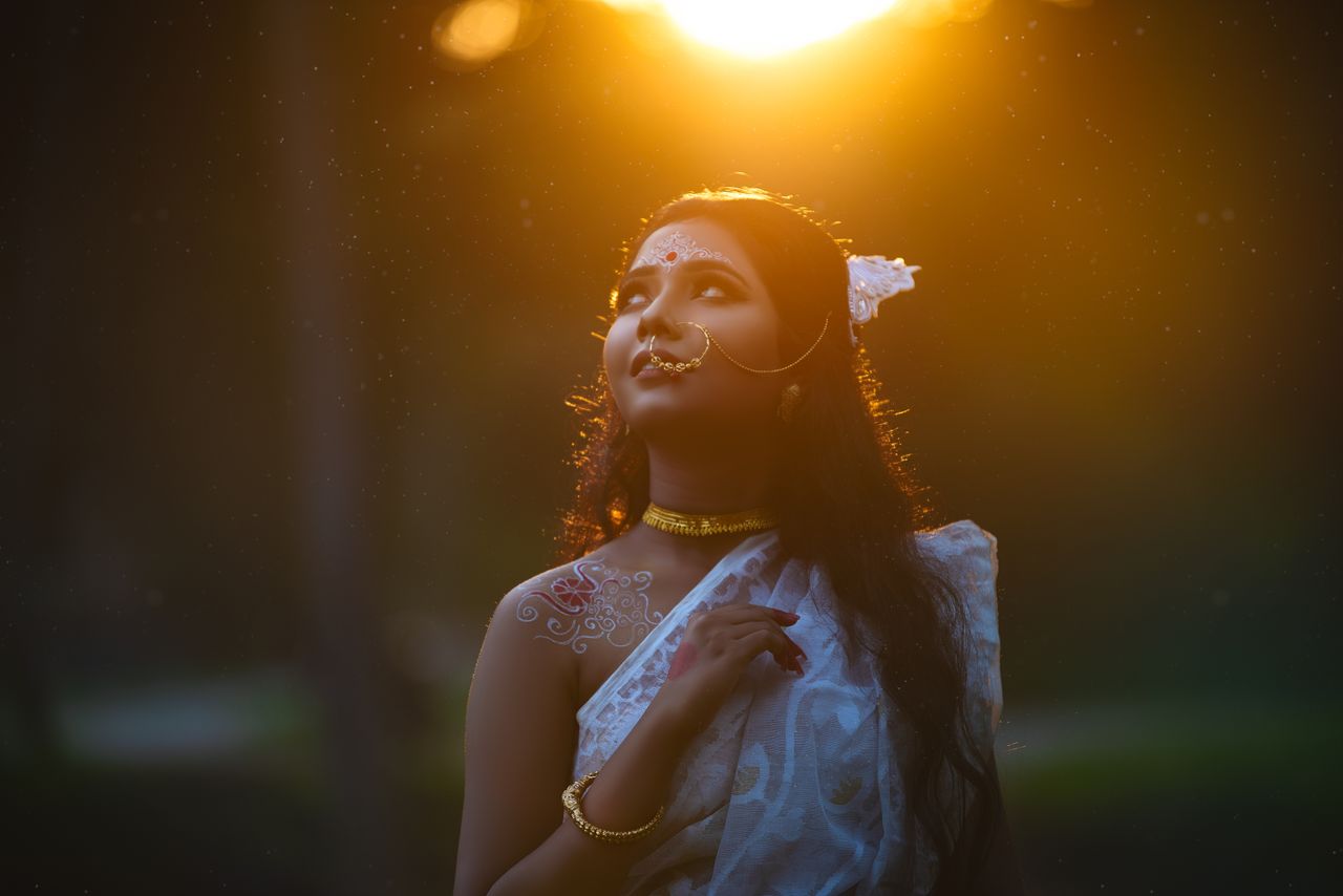 a woman wearing traditional clothing adorned with jewelry looks up tho
