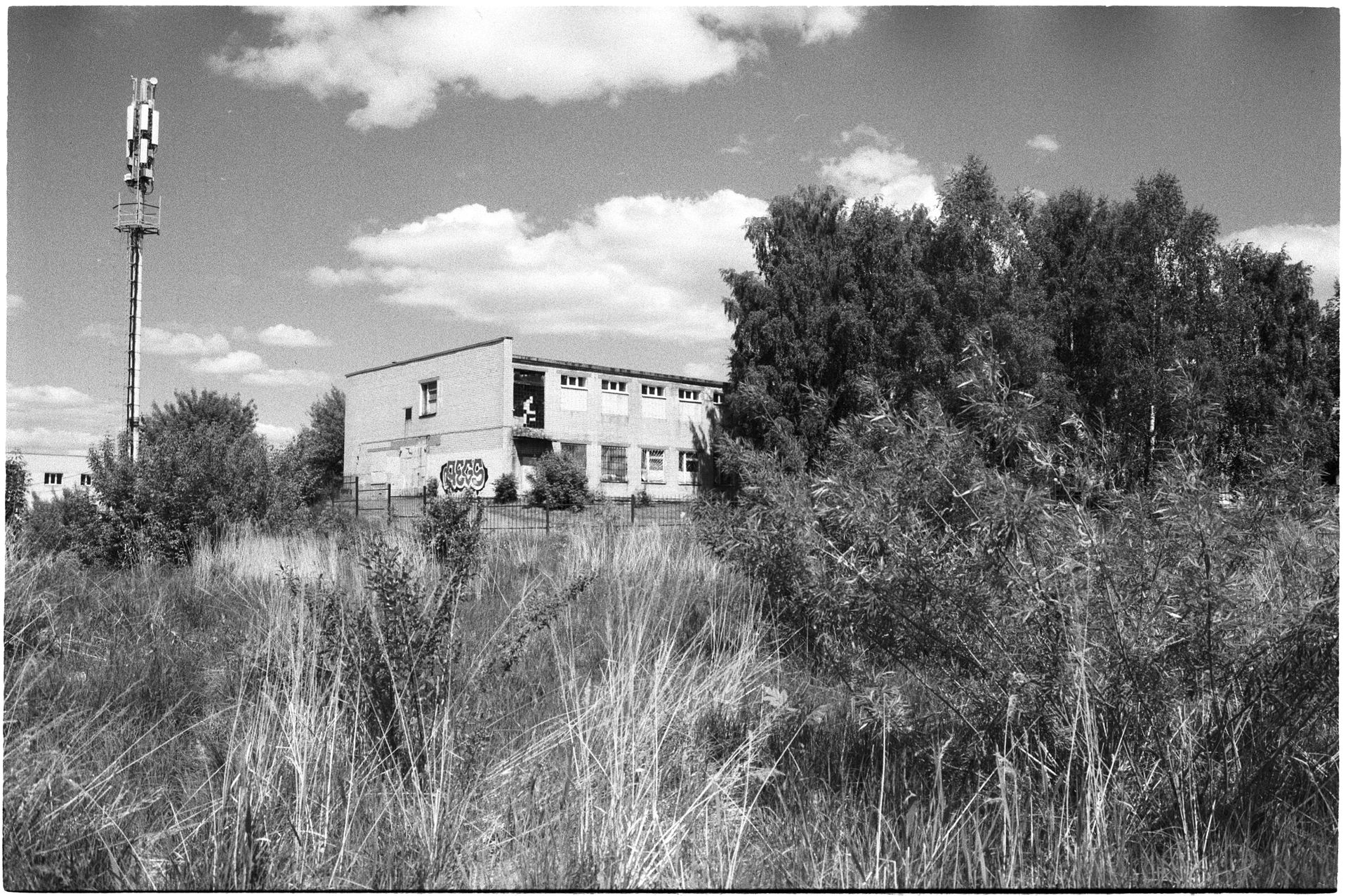 A grayscale image of an abandoned building with a cell tower and natural surroundings.