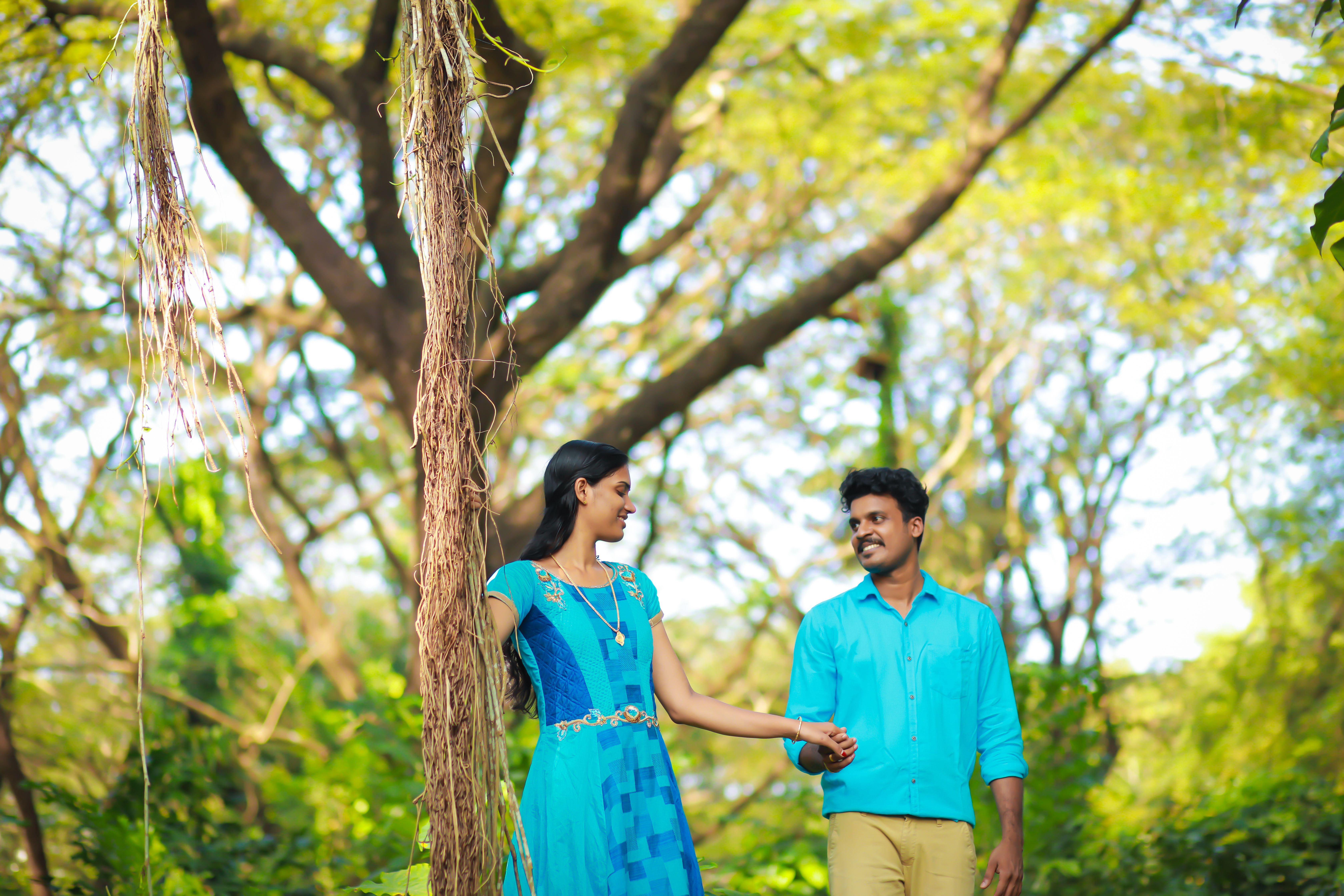 Happy couple in blue attire holding hands in a vibrant green forest, capturing a romantic moment.