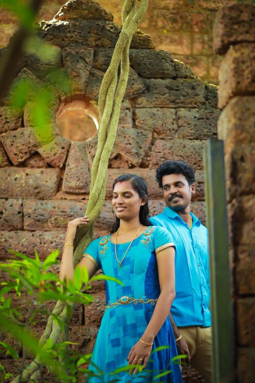 Free A couple in blue attire sharing a romantic moment amidst lush greenery and ancient stone ruins. Stock Photo