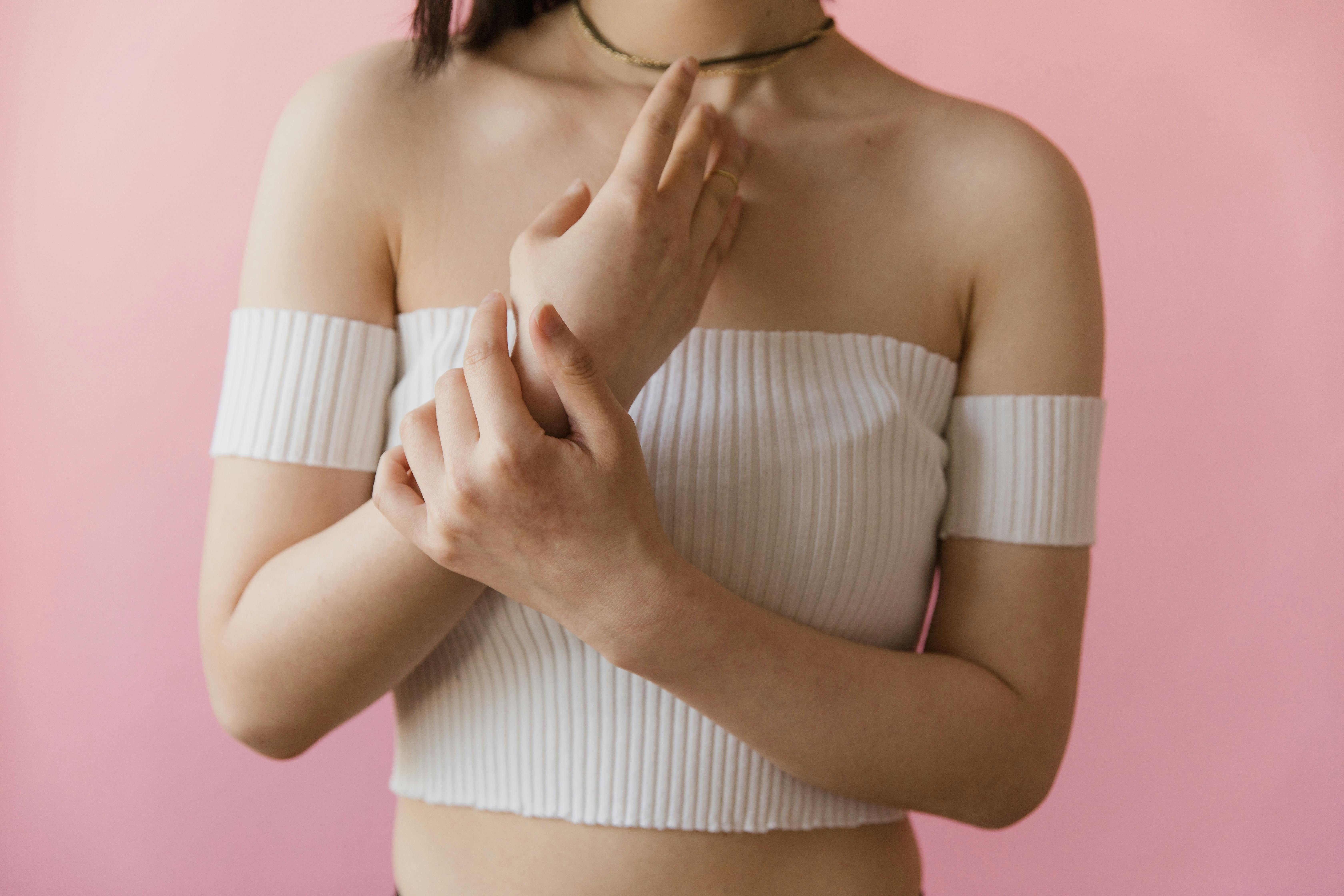 Close-up portrait of a woman posing in a white off-the-shoulder top against a pink background.