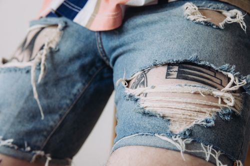 Free Detailed view of worn denim shorts with tattoos peeking through, showcasing unique style. Stock Photo