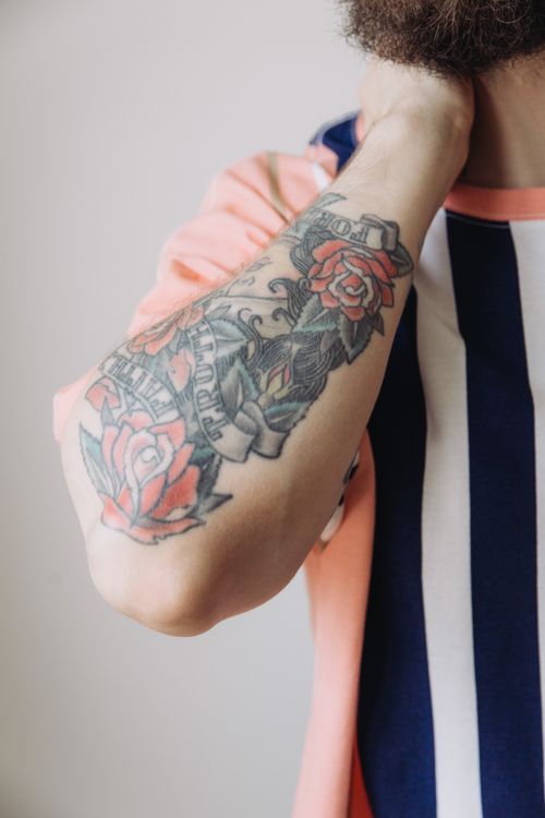Free Detailed view of colorful rose tattoo on an arm wearing a striped shirt. Stock Photo