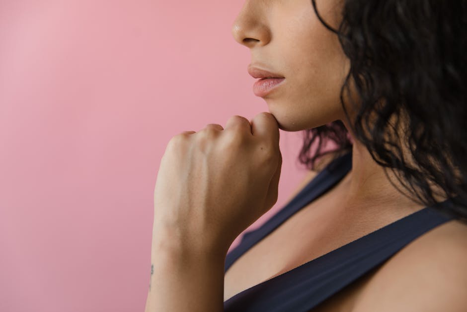 Close-up image of a woman thinking, featuring her hand supporting her chin against a pink background.