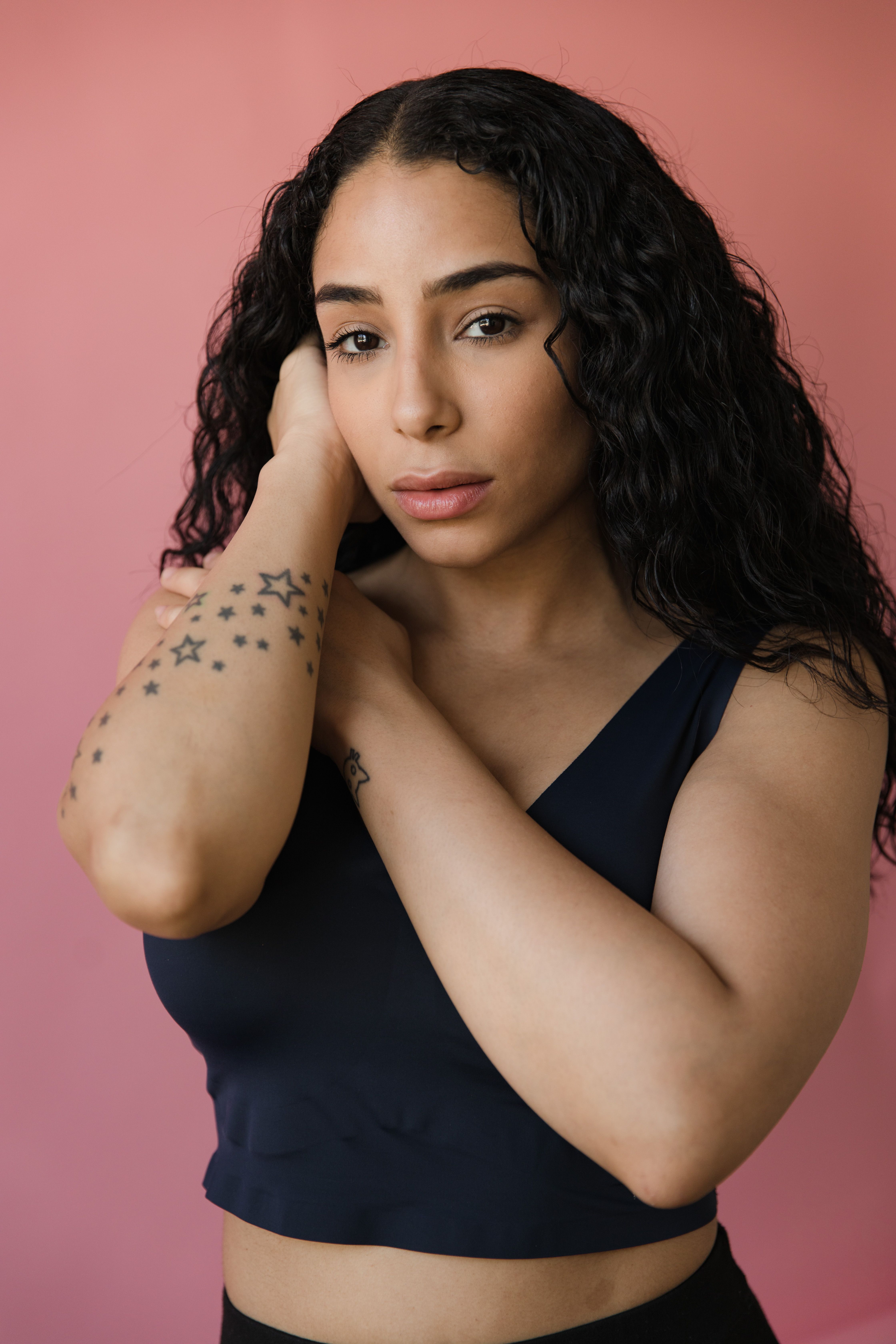 Elegant portrait of a woman with curly hair and star tattoos on a pink backdrop.