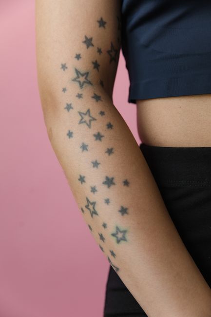 Fotomural Una foto en primer plano de un brazo con tatuajes de estrellas contra un fondo rosa.