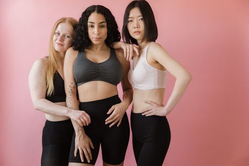 Free Three diverse women posing in activewear against a pink background, embracing fitness and body positivity. Stock Photo