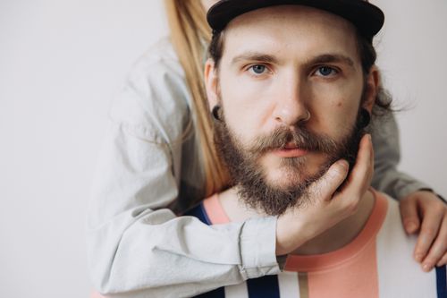 Free Close-up of a serious bearded man in a cap and striped shirt with a hand touching his face. Stock Photo