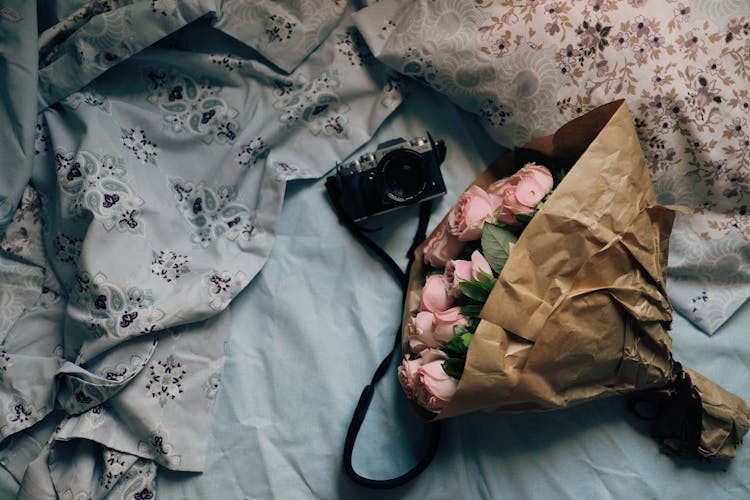 Black Camera And A Boquet Of Pink Roses On A Bed