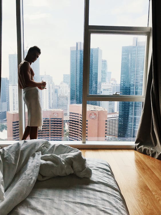 Free Man in a Towel Standing by the Window in a High Floor Apartment with View of Skyscrapers  Stock Photo