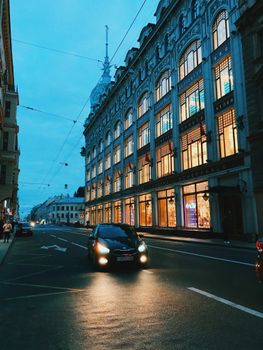 A serene night view of a bustling street in Saint Petersburg with illuminated architecture and passing cars.