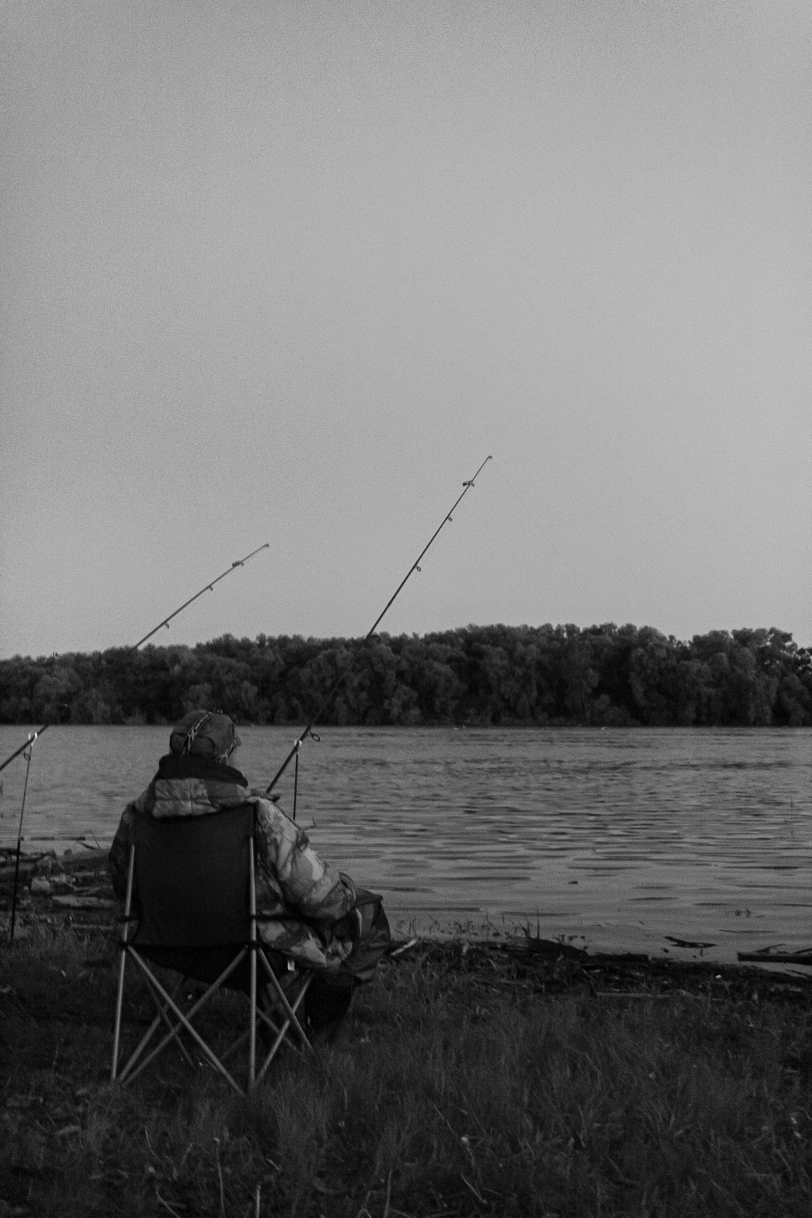 Man fishing by a lake, captured in a peaceful black and white setting.