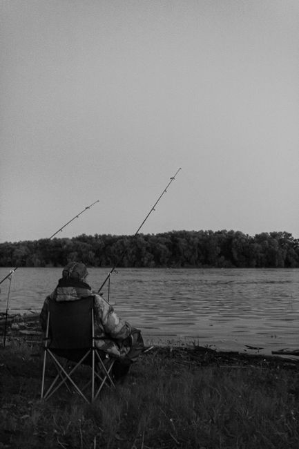 Man fishing by a lake, captured in a peaceful black and white setting.
