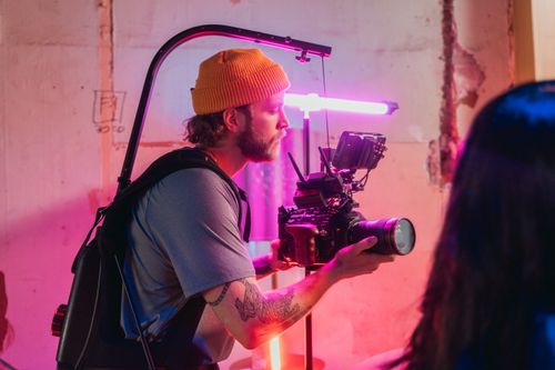 Free Cameraman operating camera on film set with colorful lighting in creative environment. Stock Photo