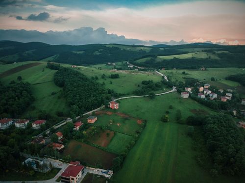 Free Aerial view of a rural landscape with lush green hills, fields, and scattered houses under a dramatic sky. Stock Photo