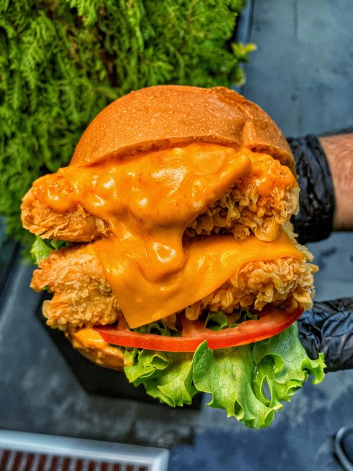 Free Close-up of a delicious cheesy chicken sandwich with fresh lettuce and tomato, perfect for a fast food meal. Stock Photo