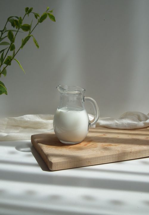 Free Elegant still life of a milk-filled glass pitcher on a wooden board in soft natural light. Stock Photo