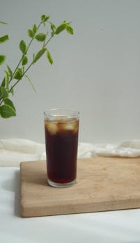A glass of refreshing iced tea with ice cubes on a wooden chopping board, indoors.