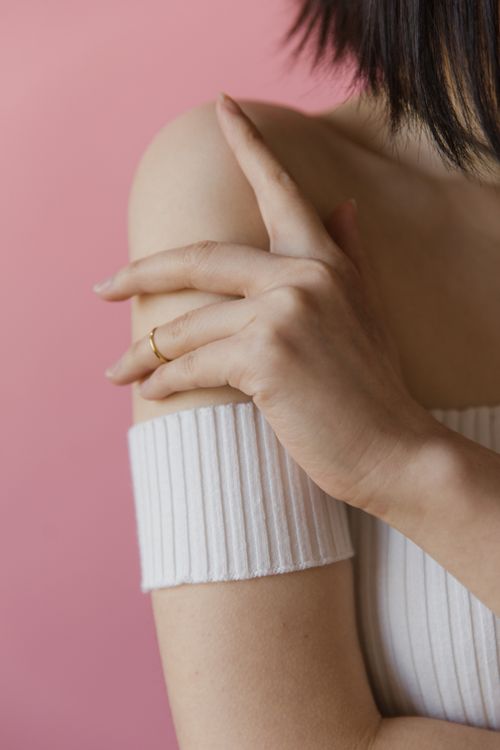 Free Close-up of a woman's hand and shoulder wearing an off-shoulder white top against a pink background. Stock Photo