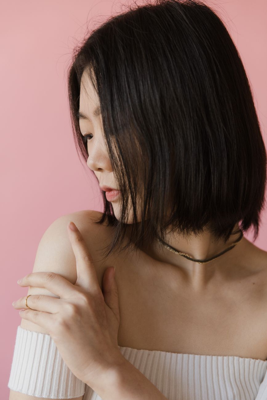 A portrait of a woman with a contemplative pose against a pink background.
