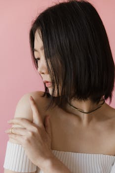 A portrait of a woman with a contemplative pose against a pink background.