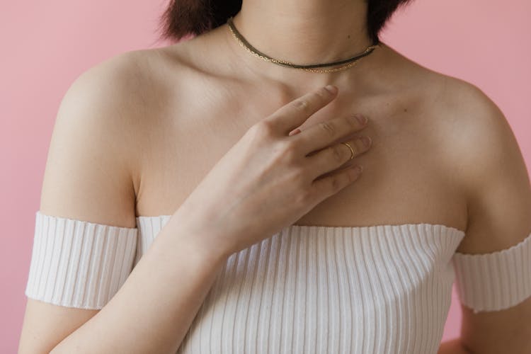 A Woman In White Off Shoulder Top With Her Hand On Her Chest