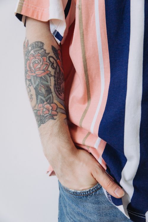 Free A close-up view of a tattooed arm resting inside a pocket with a striped shirt background. Stock Photo