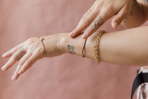 Free Close-up of a tattooed arm wearing elegant gold bracelets and rings on a soft background. Stock Photo