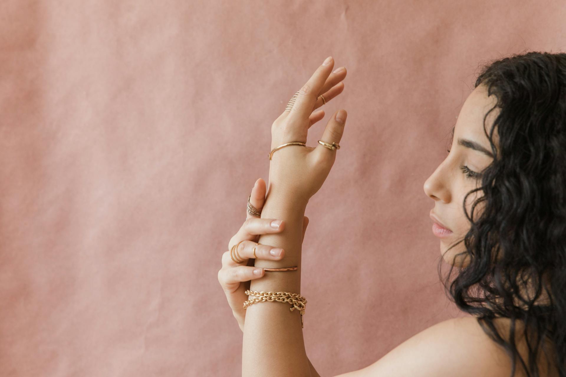 Close-up of a woman with gold jewelry against a pink background, highlighting elegance and style.