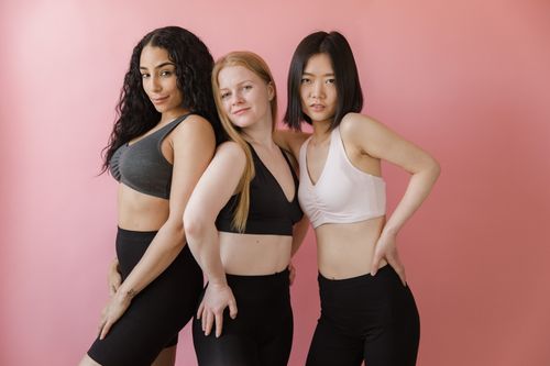 Free Three women in athletic wear confidently pose against a pink backdrop, showcasing diversity and fitness. Stock Photo