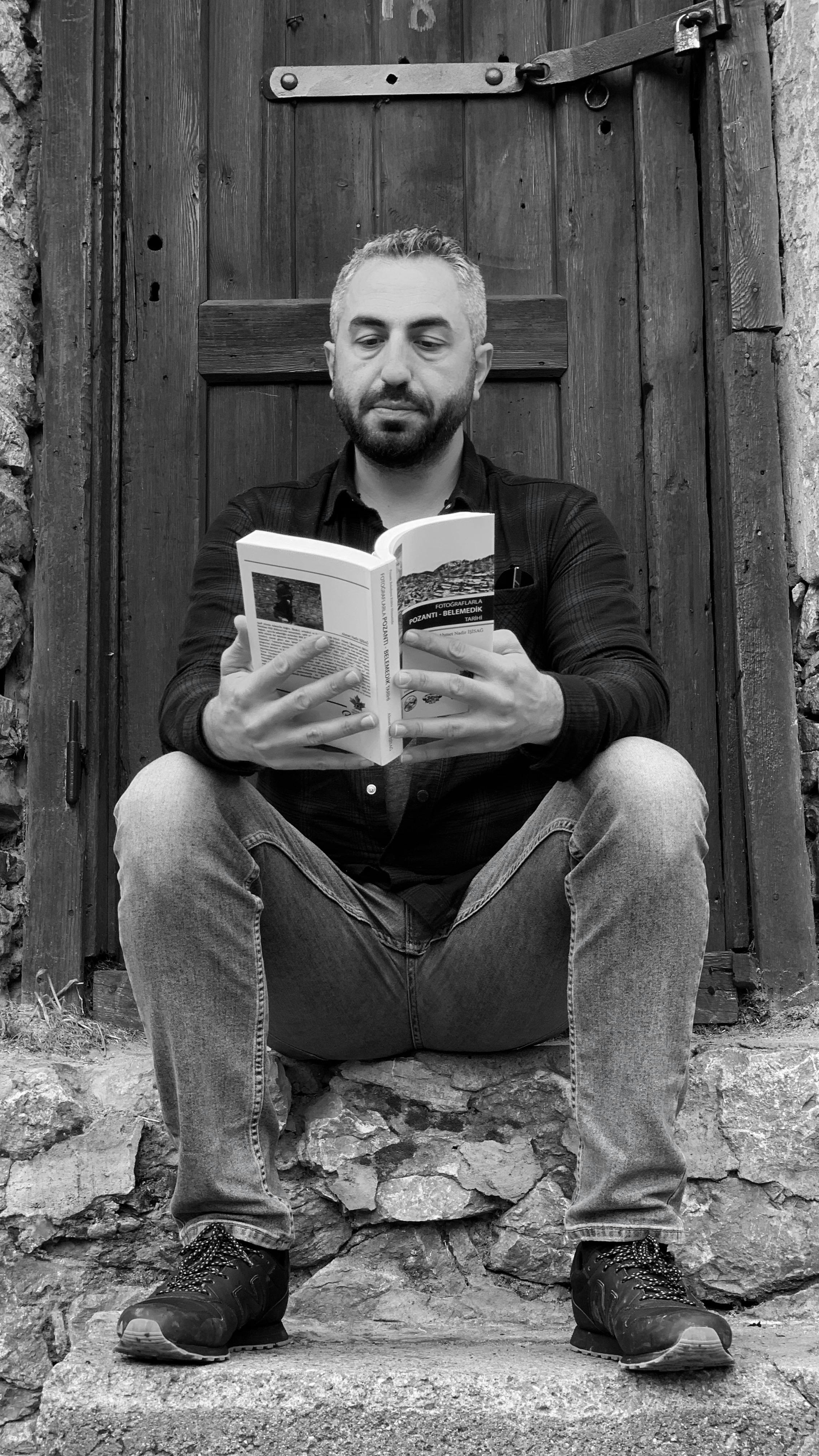 Middle-aged man enjoying a book while seated on rustic stone steps. Black and white photography.