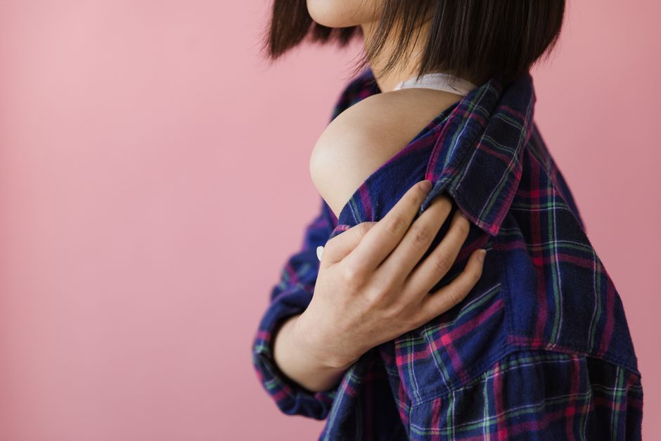 Close-up of a woman slightly exposing shoulder, wearing a plaid shirt against a pink background.