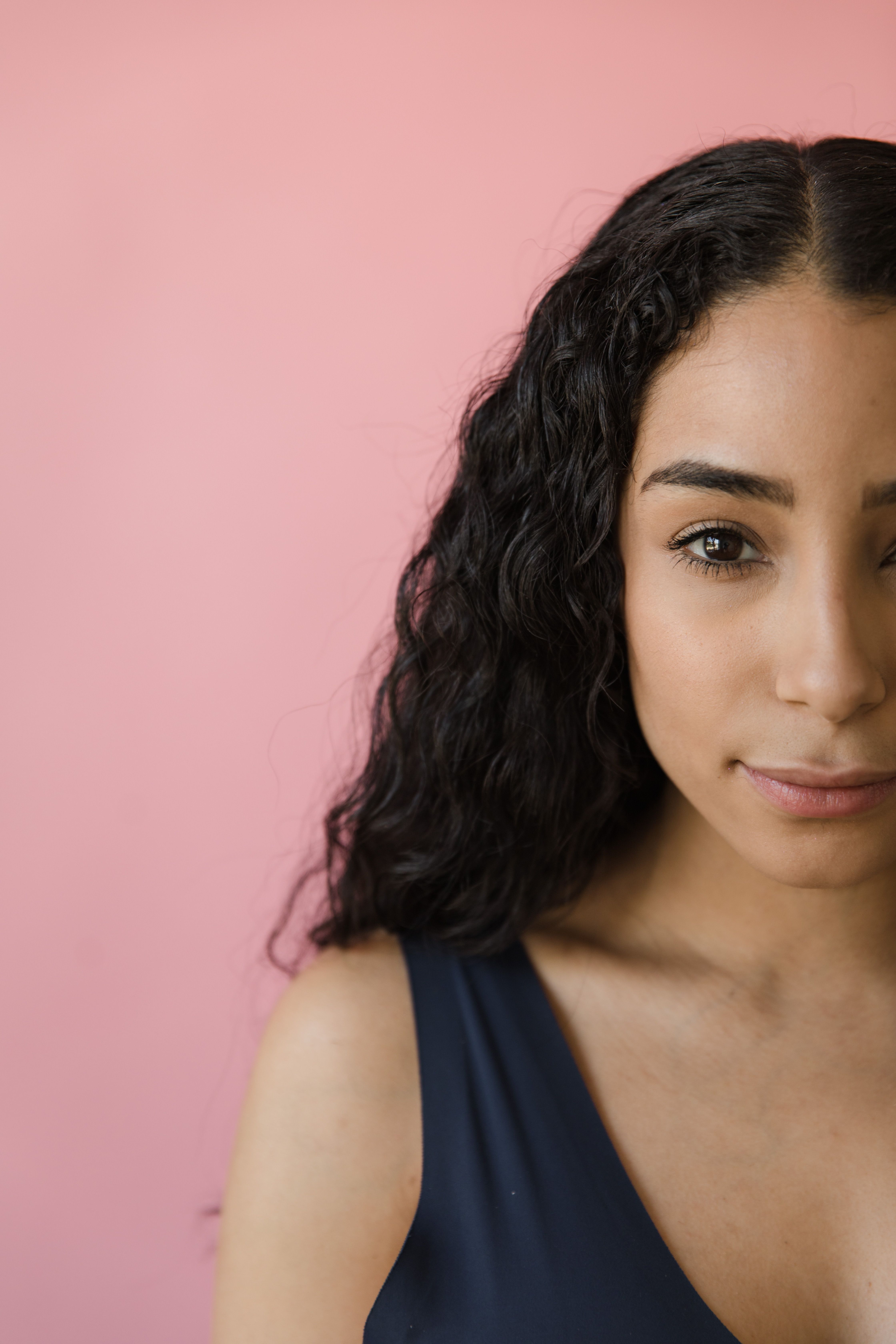 A close-up portrait of a young woman with curly hair against a pink background.